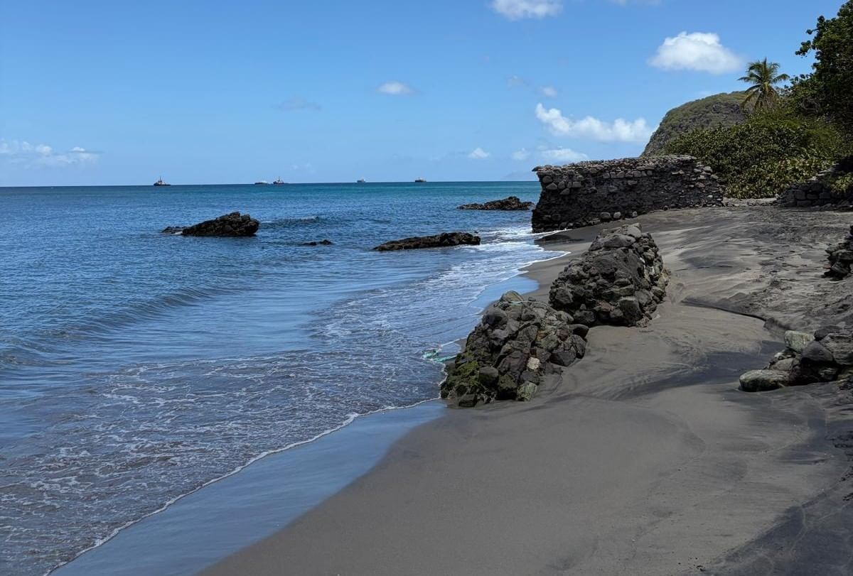 Volcanic black sand beach with natural rock formations along calm ocean water near Golden Rock Resort