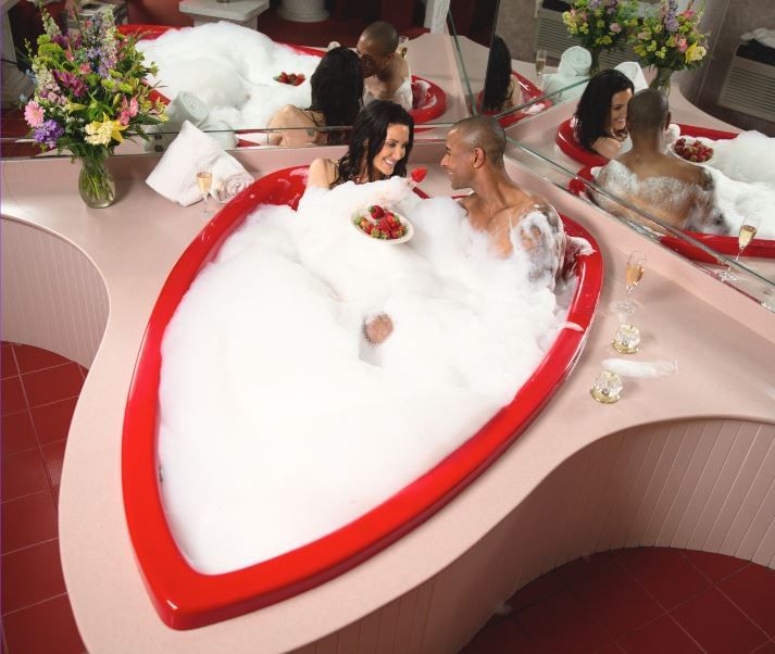 A couple enjoys a romantic bubble bath in a heart-shaped tub with strawberries and champagne at Cove Pocono Resorts