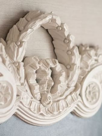 Detailed carving on an ornate white headboard under a textured wall in Balcony Suite at Warwick San Francisco
