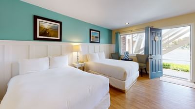 Two beds with table lamp by the opened door and seating area in Two Double at Breezeway Boutique Hotel