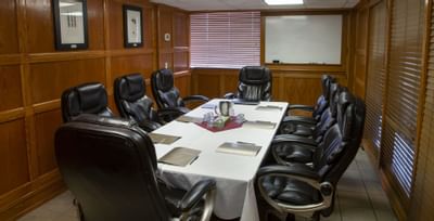 Black leather chairs by a linen table with notepads, under a wall-mounted whiteboard at Glenmore Inn & Convention Centre