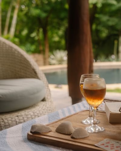 Dos cócteles y conchas marinas en una bandeja de madera junto a la tranquila piscina del Morgan's Rock Reserve & Ecolodge.