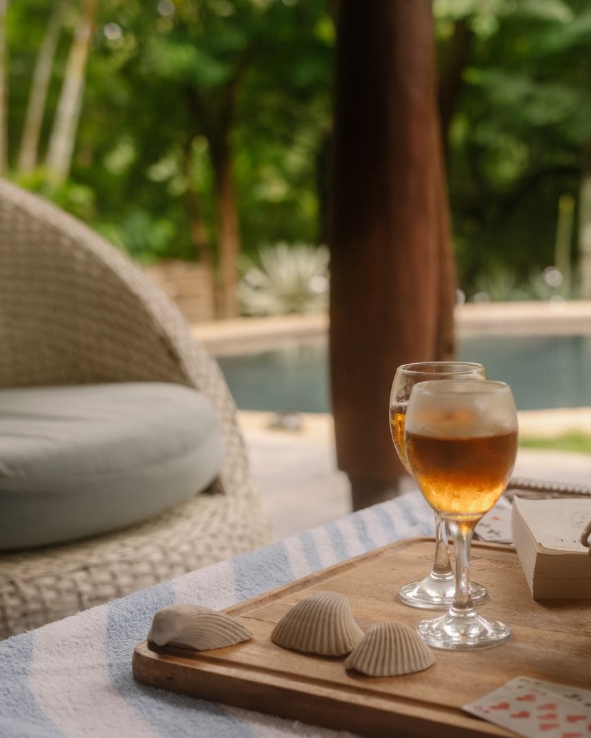 Dos cócteles y conchas marinas en una bandeja de madera junto a la tranquila piscina del Morgan's Rock Reserve & Ecolodge.