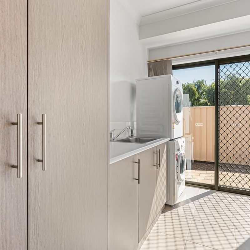 Clean laundry room with washing machine, cabinets, and sliding glass door at La Trobe University Regional Housing – Mildura.