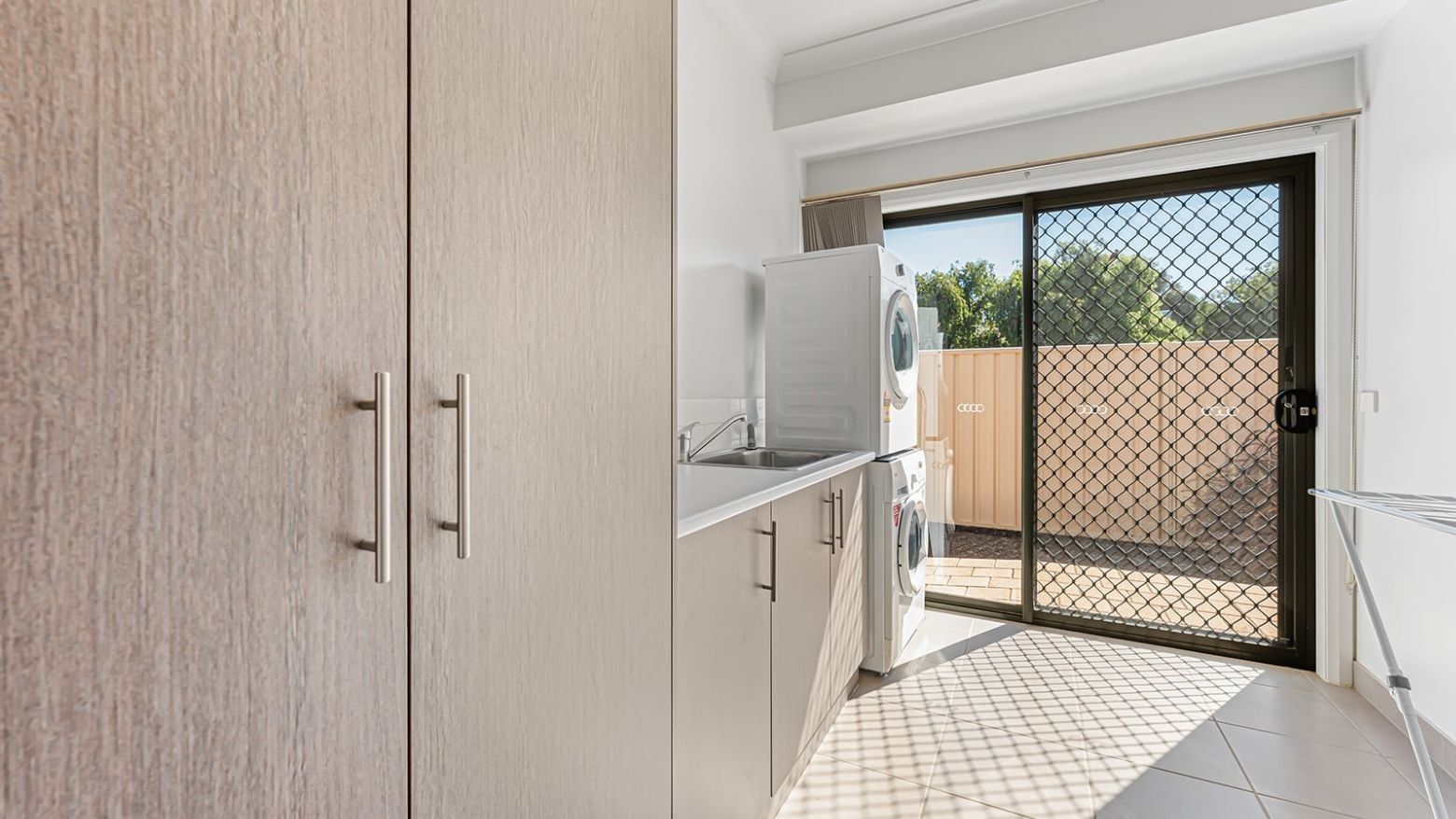 Clean laundry room with washing machine, cabinets, and sliding glass door at La Trobe University Regional Housing – Mildura.