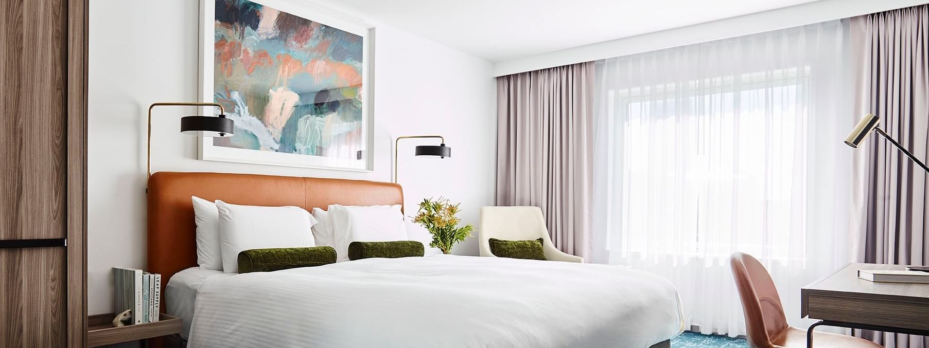 A modern bedroom with a large bed, desk, chair, artwork, and blue rug.