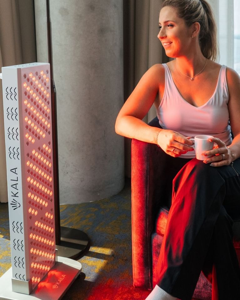 Woman relaxing with red light therapy panel while holding a cup in a yoga room