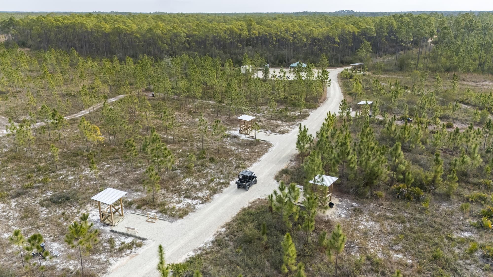 Aerial view of a dirt road in a forest with small wooden structures and a vehicle.