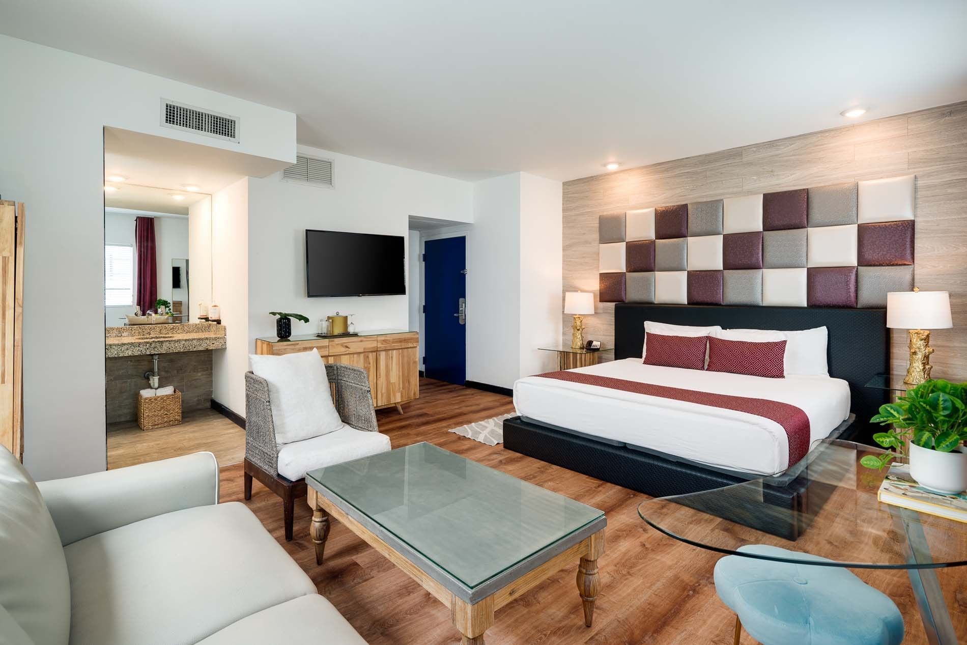 A wide view of a hotel suite with a bed, sofa, coffee table, armchair, and TV