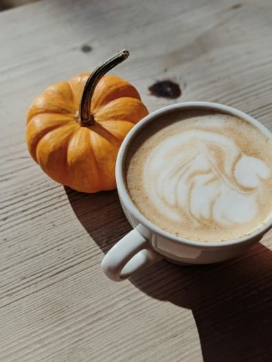 A small pumpkin next to a mug of coffee. A pumpkin treat in Orlando is the pumpkin spice latte from Craft & Common.