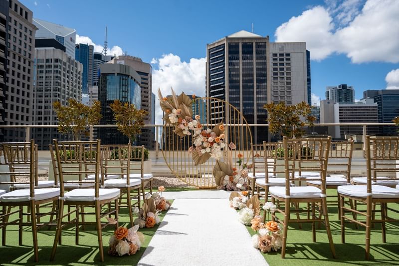 Outdoor wedding setup with chairs and floral arch against a cityscape at Sofitel Brisbane Central
