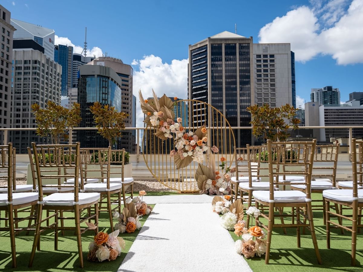 Outdoor wedding setup with chairs and floral arch on a rooftop with city skyline background at Sofitel Brisbane Centraldings