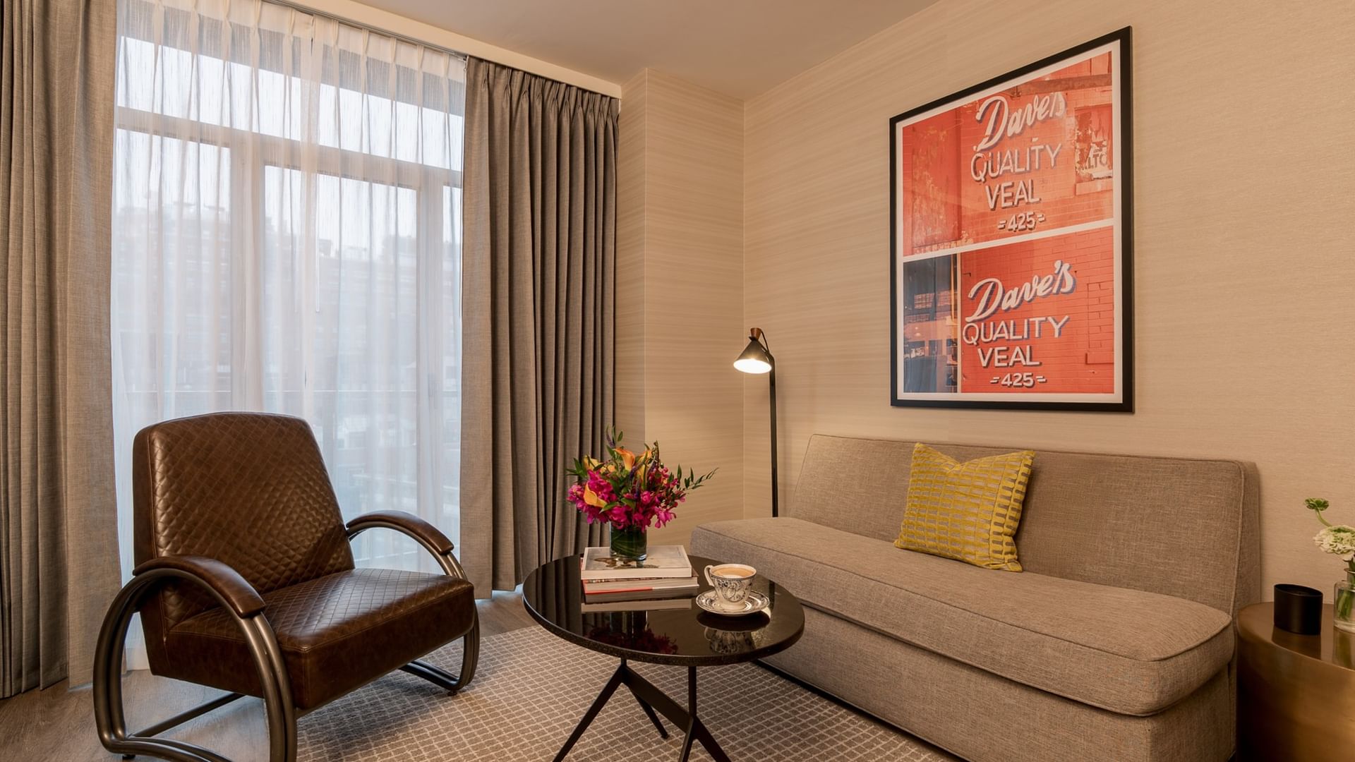 Two-Bedroom Manhattan Suite living area with beige sofa, vintage chair, and retro artwork at Gansevoort Meatpacking NYC.
