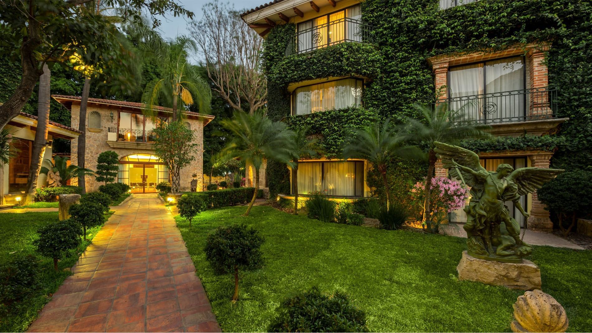 Lush ivy-covered exterior with garden paths and an angel statue at Quinta Real Guadalajara