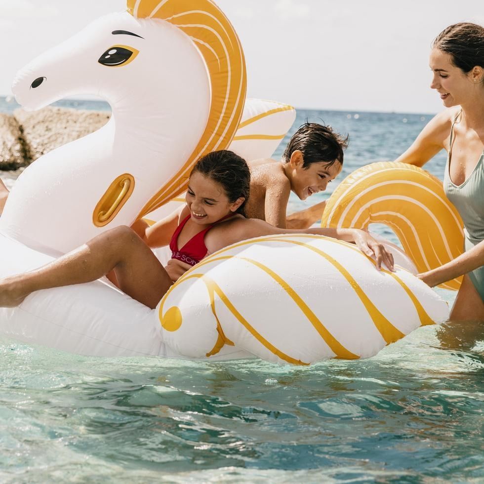 Zwei Kinder und eine Frau auf einem aufblasbaren Seepferd im Wasser entspannend.