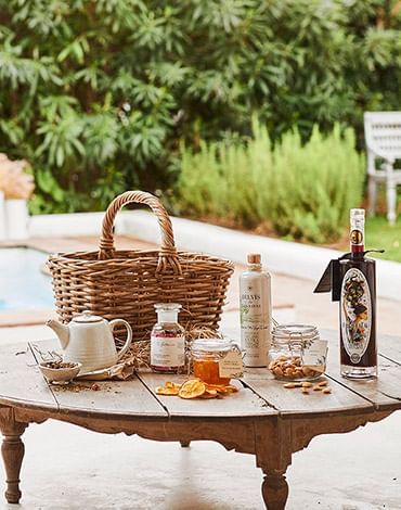 Close-up of a rustic outdoor table at Marbella Club set with a picnic basket, gourmet preserves, and olive oil