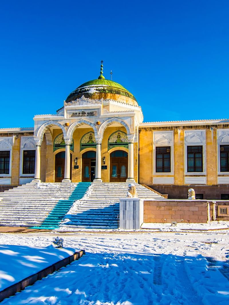 The Ethnography Museum of Ankara with snow-covered ground and a flag on a clear day.