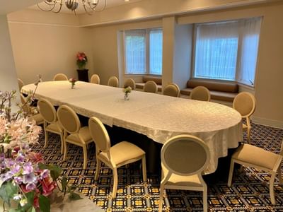 Long oval table with a tablecloth surrounded by padded chairs beside flower vases in Penwood at The Simsbury Inn
