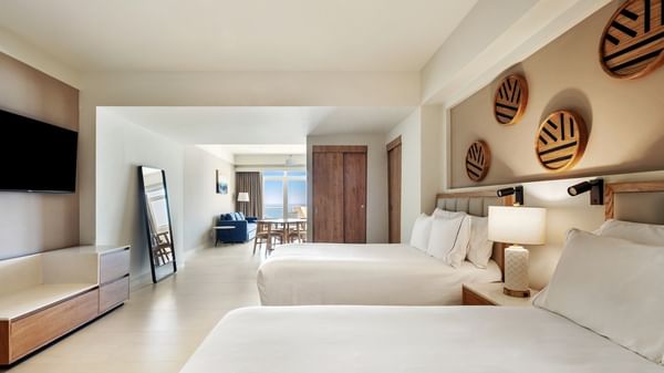 Junior suite vista frontal Al Mar with two white beds, wooden wall decor, and a distant ocean view at Sunvivia Mazatlán