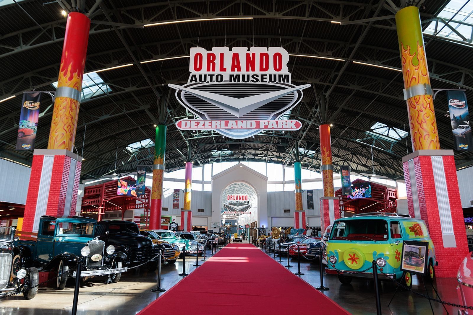 A long red carpet beneath a sign that says Orlando Auto Museum Dezerland Park with vintage cars parked along either side.
