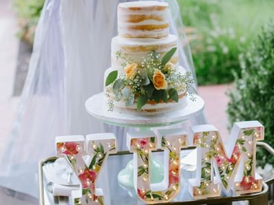 Three-tier naked wedding cake with peach roses on stand with illuminated YUM letters at Aramark Chauncey Conference Center