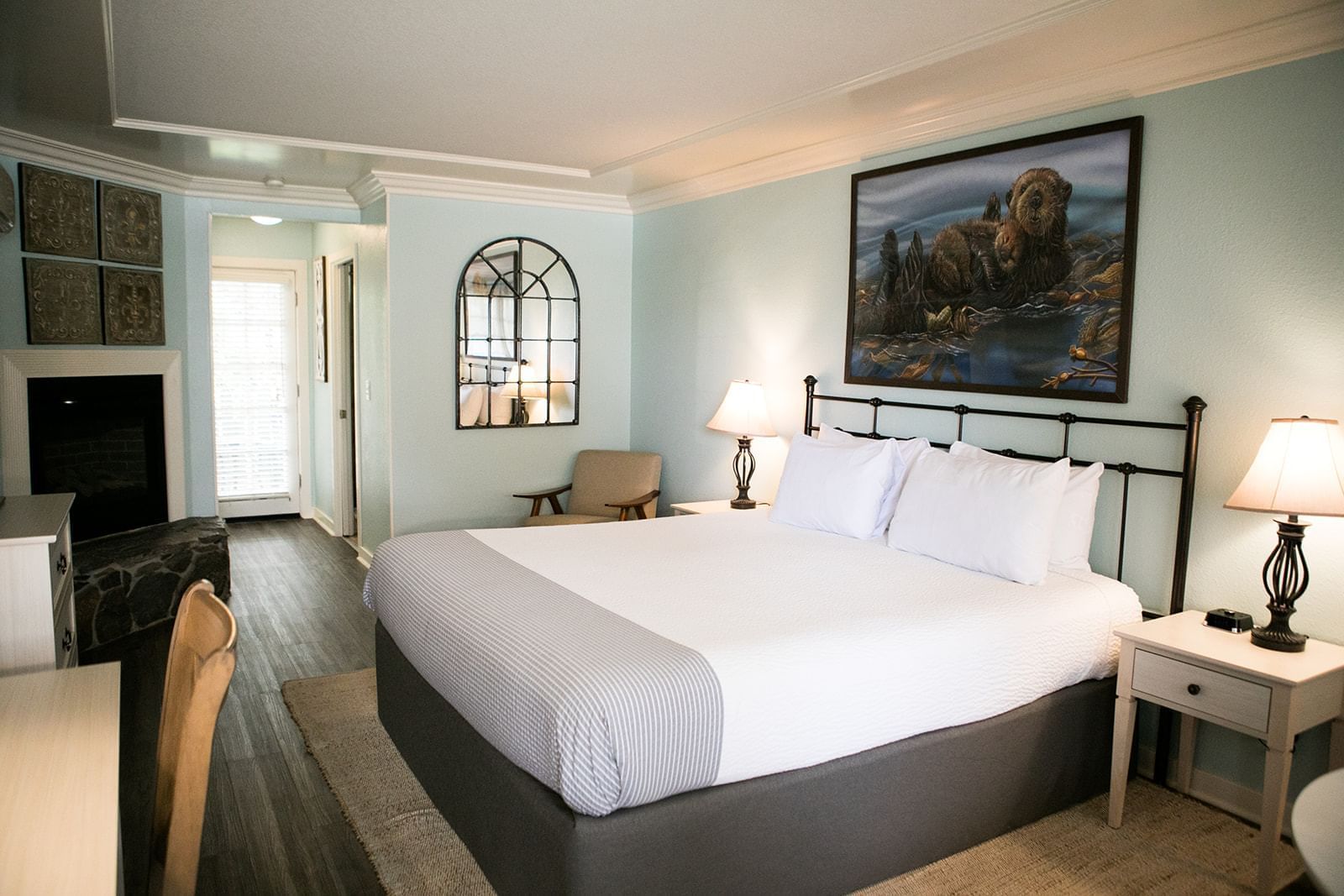 A wide-angle view of a hotel room with a large bed, nightstands, lamps, a painting, and a fireplace.