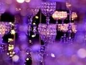 Close-up of crystal event chandeliers reflecting purple and golden ambient lighting in a dark room at The Sebel Brisbane