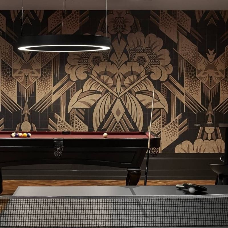 A room with a pool table, decorative wall, small table with glass, and ping pong table.