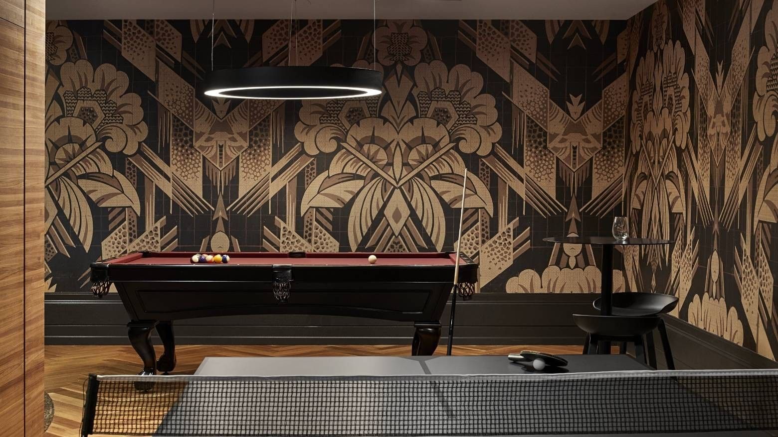 A room with a pool table, decorative wall, small table with glass, and ping pong table.