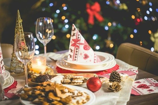 A festive table prepared for a Christmas meal with twinkling lights in the distance.