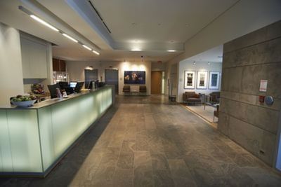 Reception area with a long illuminated counter, stone flooring, and seating space at the Schulich School of Business.