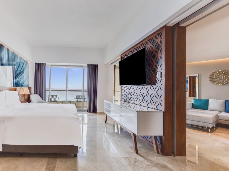 Bedroom with bed, TV, large windows and slight view of living area at Live Aqua Cancún