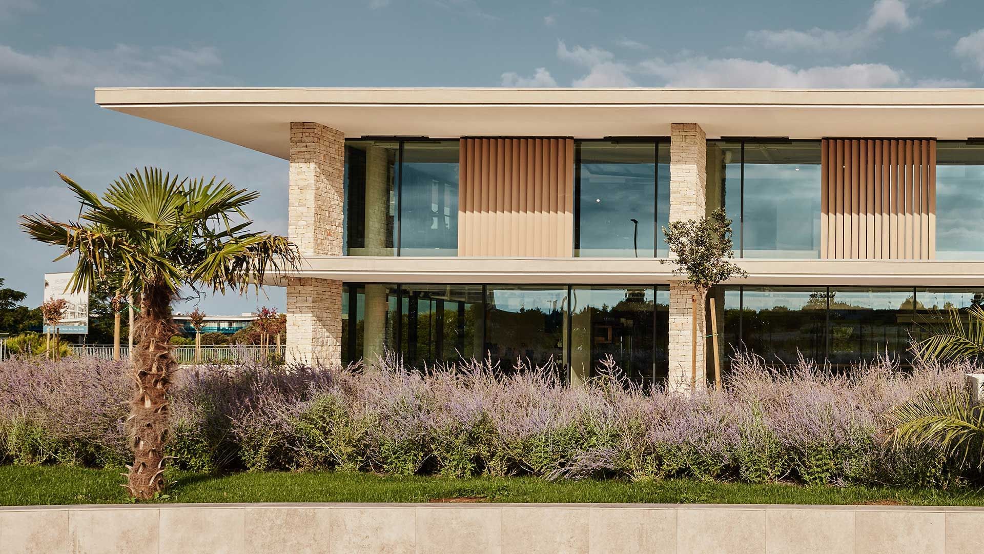 Modern two-story building surrounded by lush trees under a blue sky at Falkensteiner Hotel & Spa Iadera