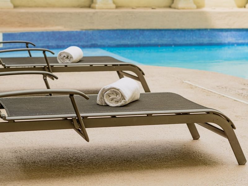 Rolled towels on sunbeds by the pool at Gamma Hotels