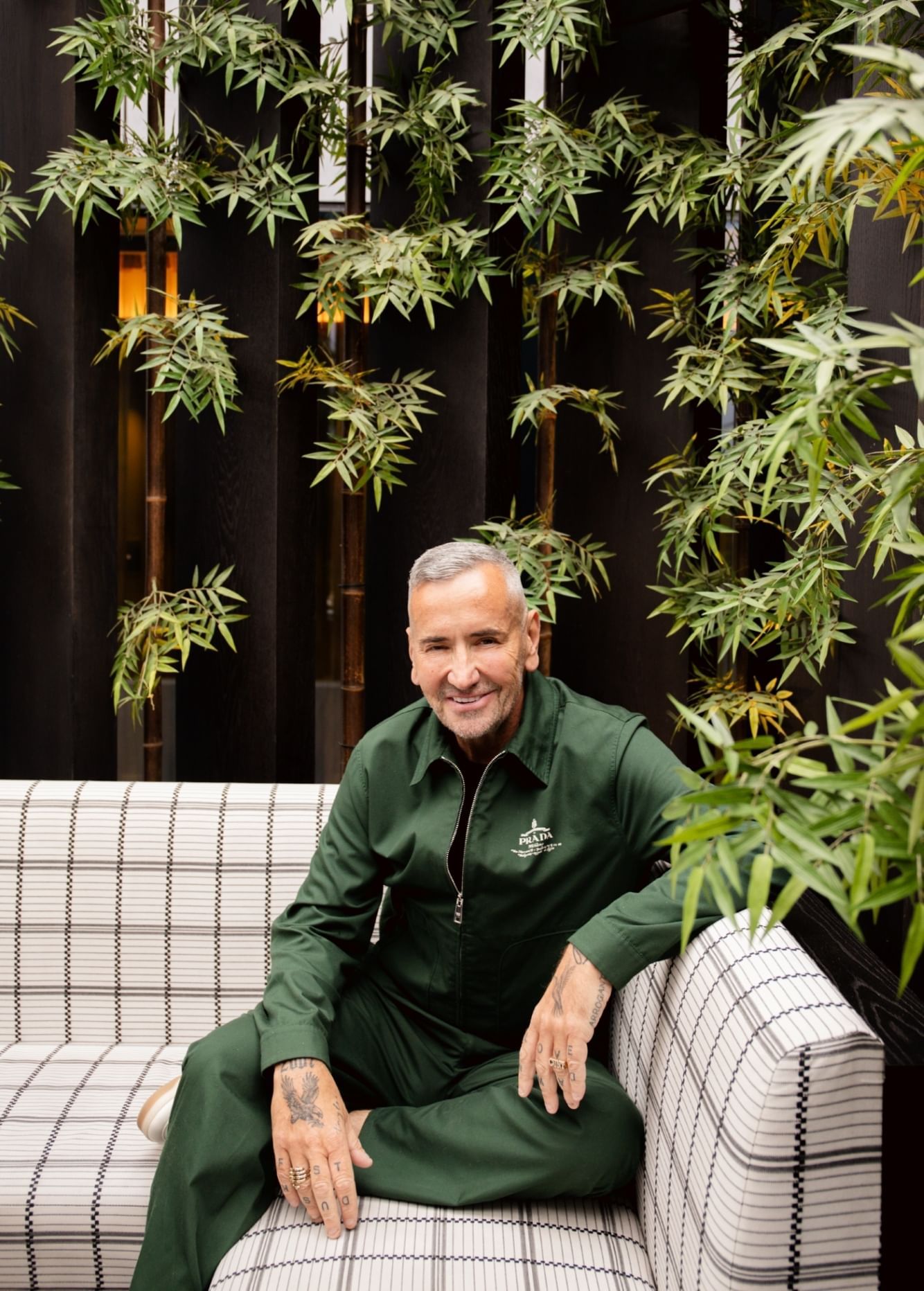 A man sitting on a couch surrounded by green plants at The Londoner Hotel