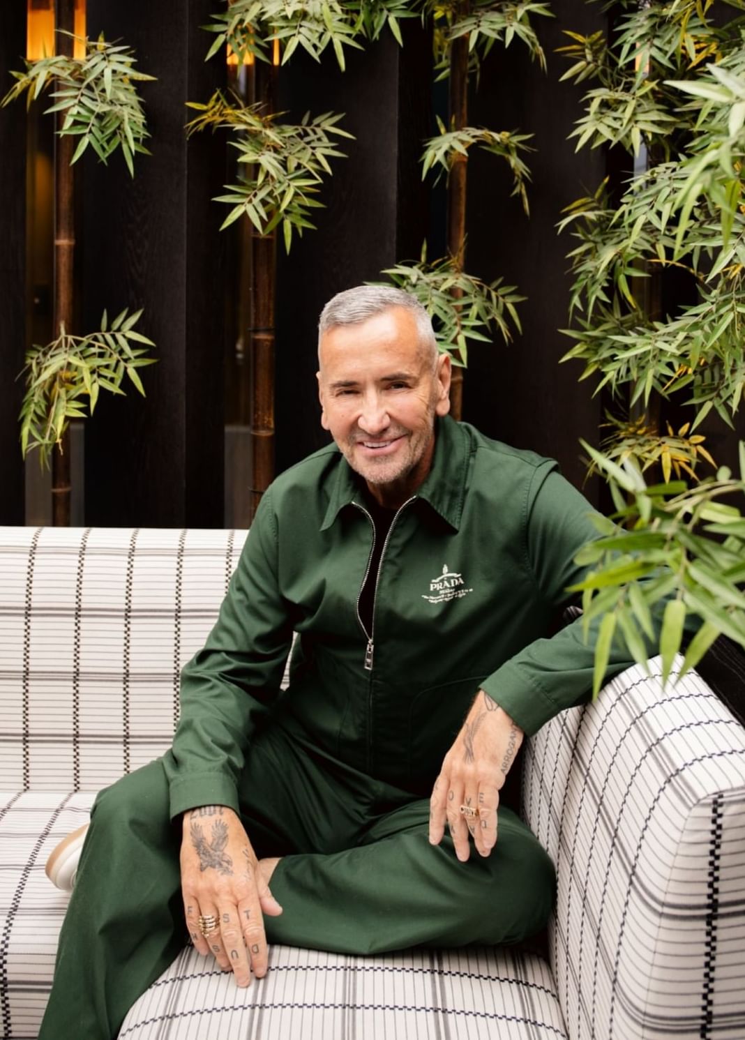 A man sitting on a couch surrounded by green plants at The Londoner Hotel