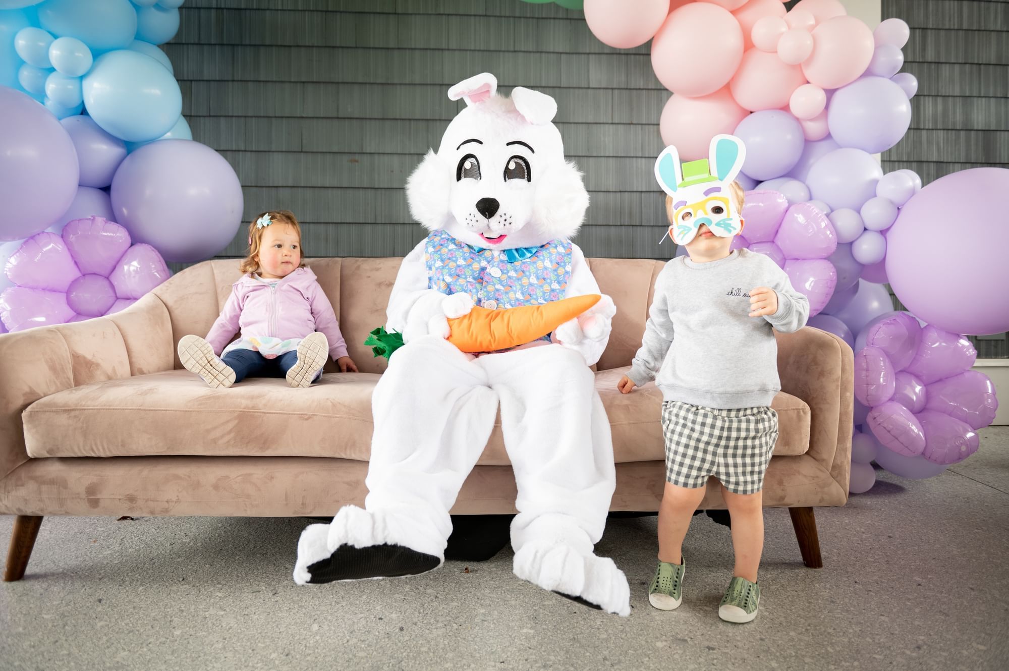 A bunny mascot poses with two young children in front of colorful balloon decorations.
