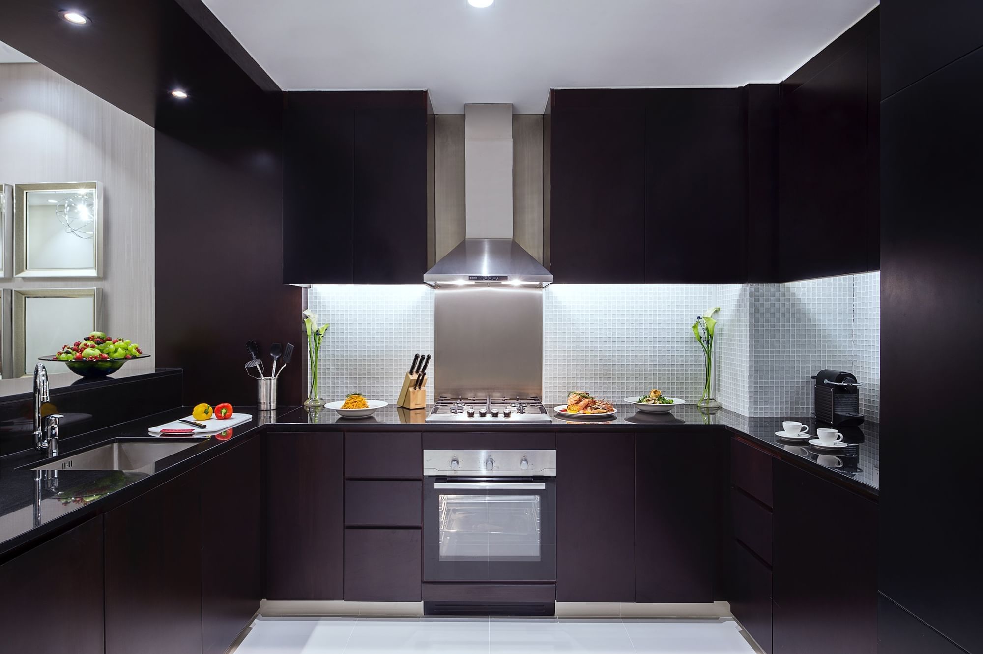 Kitchenette with black cabinets and stainless steel appliances in One Bedroom Suite at DAMAC Maison Distinction