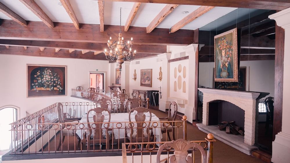 Indoor balcony dining in Tierra Mia featuring wooden beams, a chandelier, and a cozy fireplace at Quinta Real Zacatecas