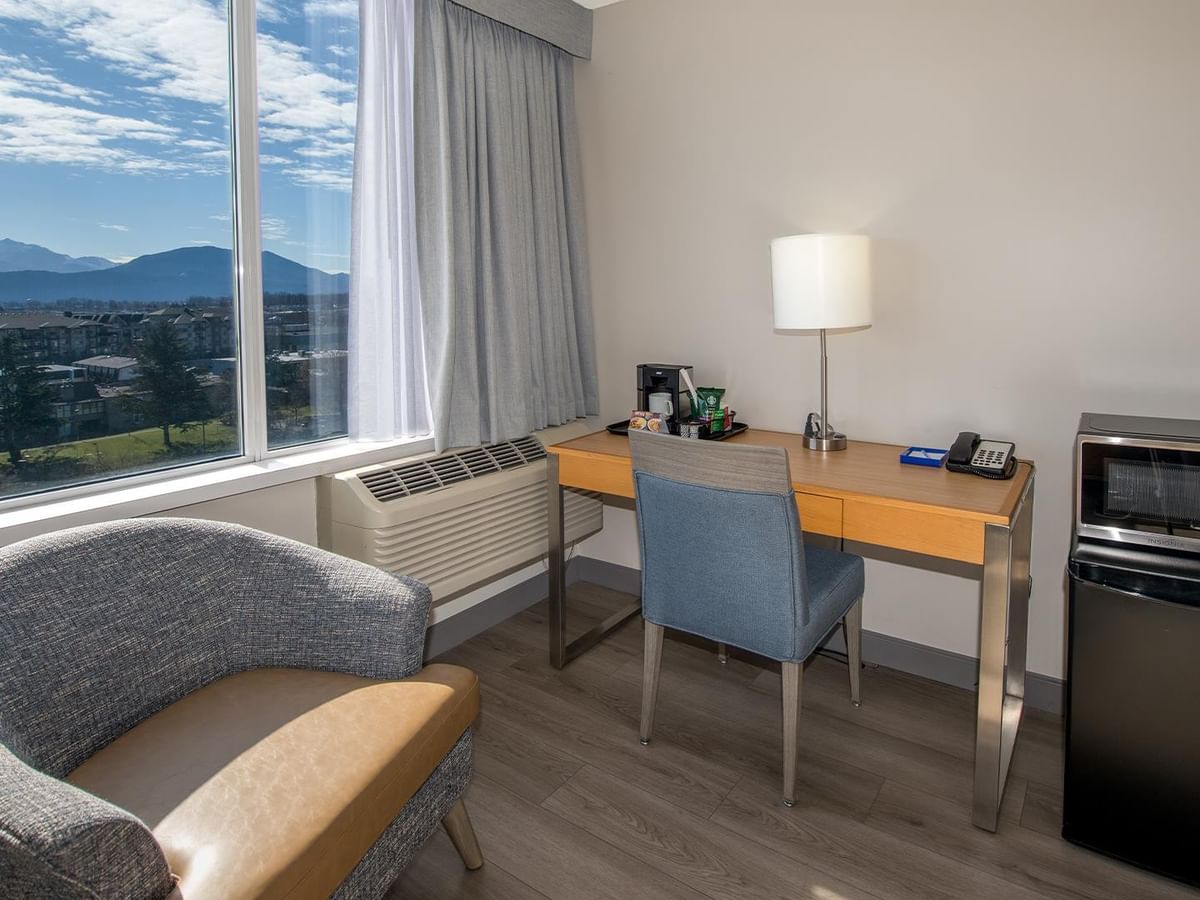 A hotel room with a desk, chair, refrigerator, and pond view.