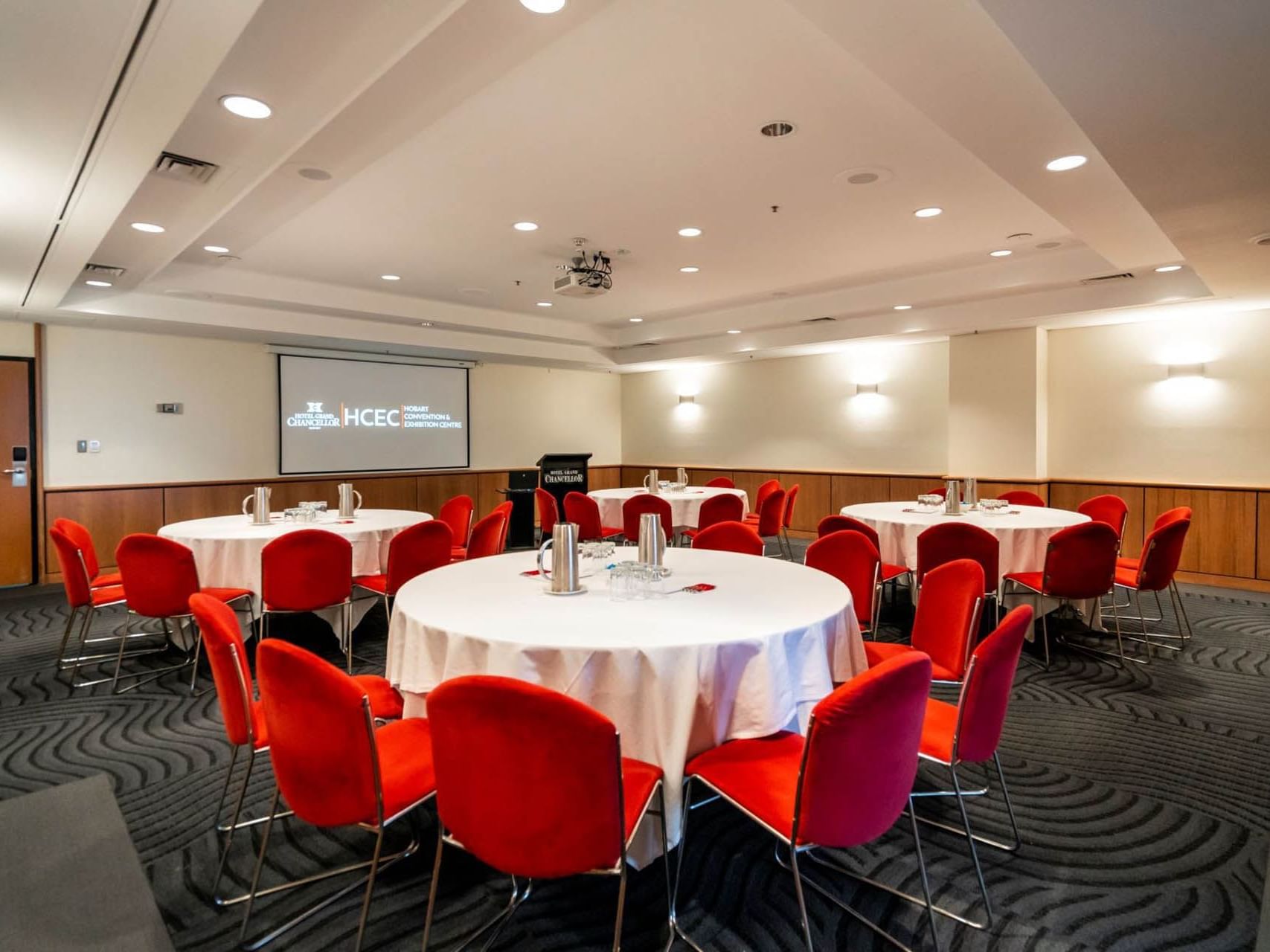 Banquet set-up with red chairs and white tables and a projector in Chancellor 4 at Hotel Grand Chancellor Hobart