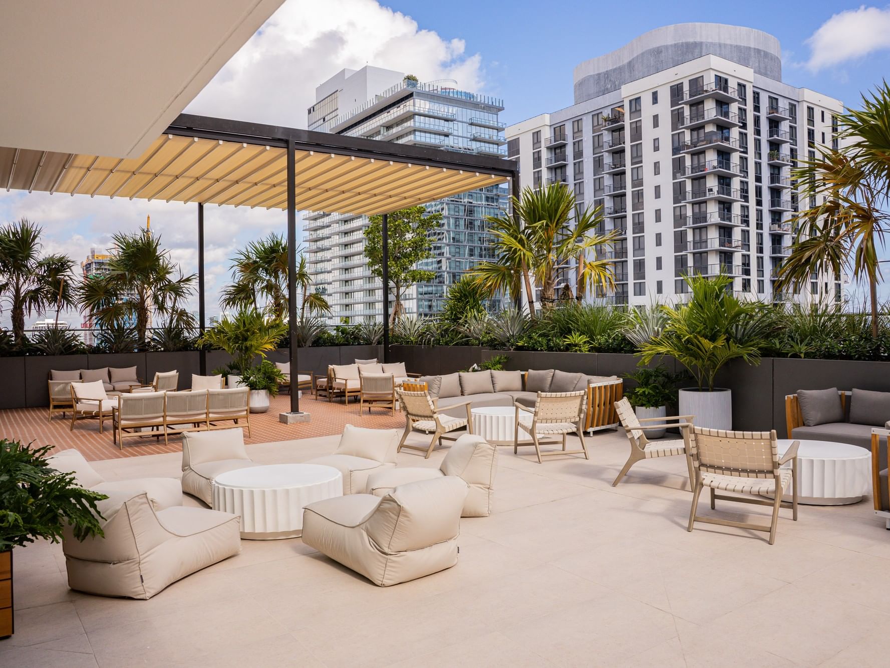Upscale Rooftop Pool Deck featuring cream lounge seating, a pergola, and city skyscrapers at The Crosby Miami World Center
