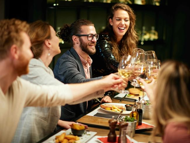 Group of friends enjoying a wine toast, featuring a vibrant dinner setting with gourmet food at Anne d'Anjou