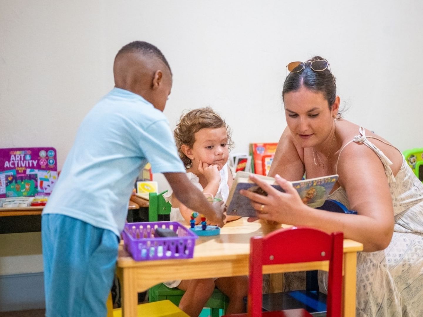 Woman reading a book to two children at a small table in a playroom at Savannah Beach Hotel.