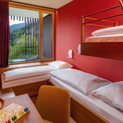 Camera con due letti a castello, un letto singolo, tavolo con giochi, e una vista su una terrazza.