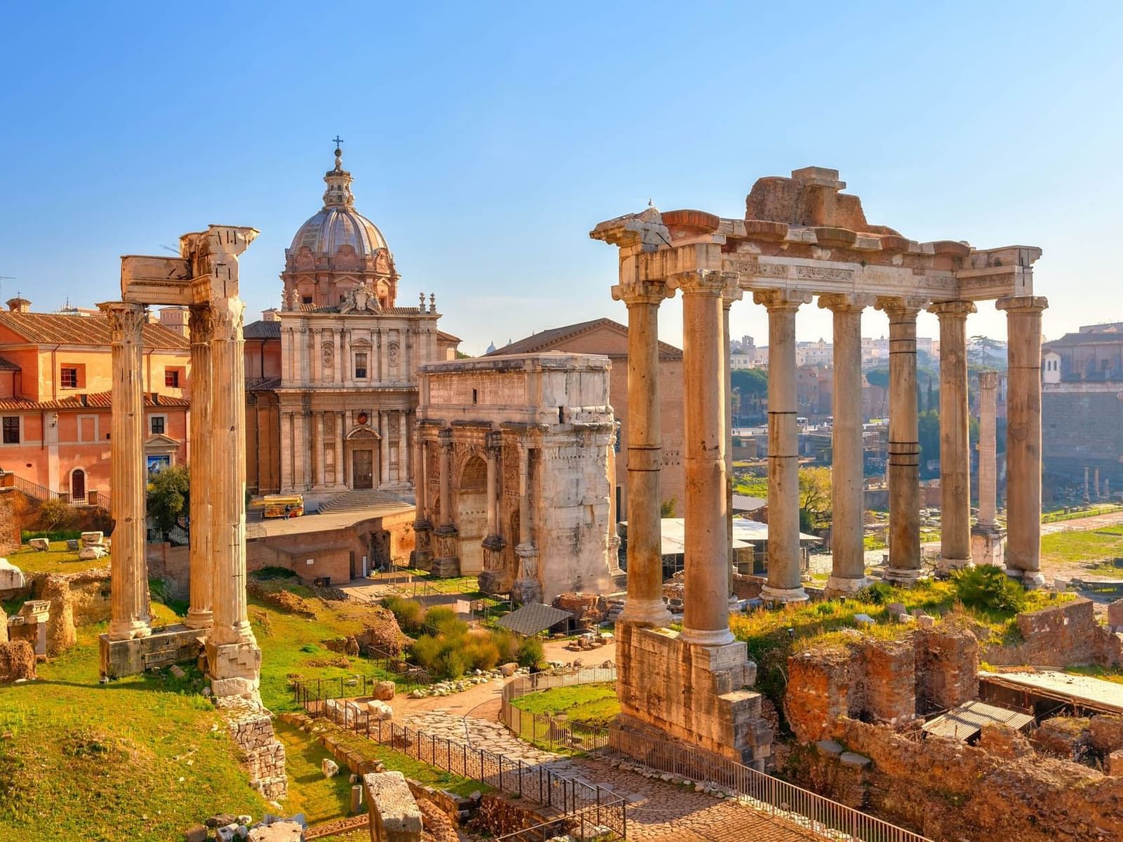 Scenic view of the Roman Forum, with ancient columns and lit buildings beneath a vibrant sky near The Guardian Hotel