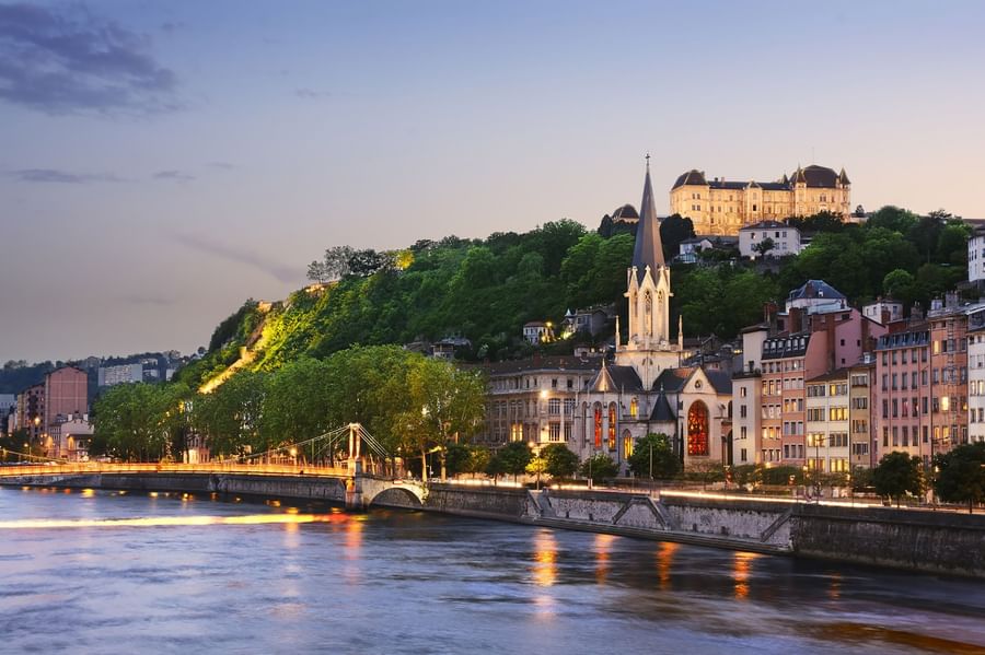 Scenic city view with a historic church and colorful buildings along a calm river near Warwick Reine Astrid - Lyon