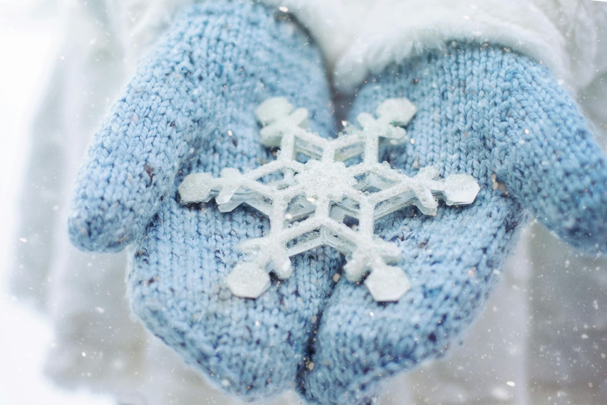 Two light blue mittens hold a large white snowflake. 