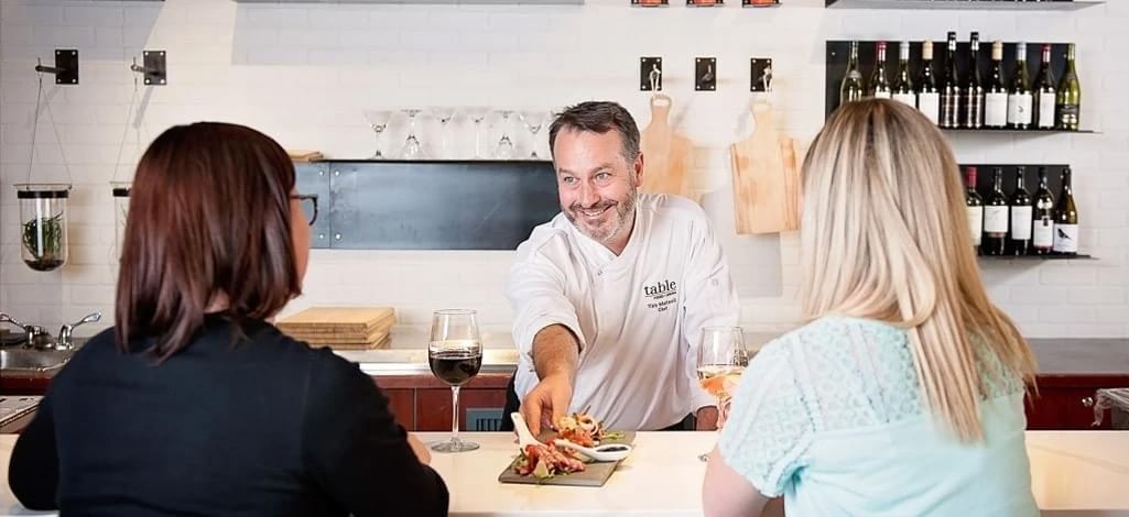 A chef serves an appetizer to a couple sitting at the bar of a Canmore dinner restaurant.