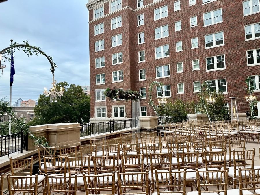 Gold chairs in rows by a floral arch under a chandelier on the rooftop at Warwick Melrose Dallas